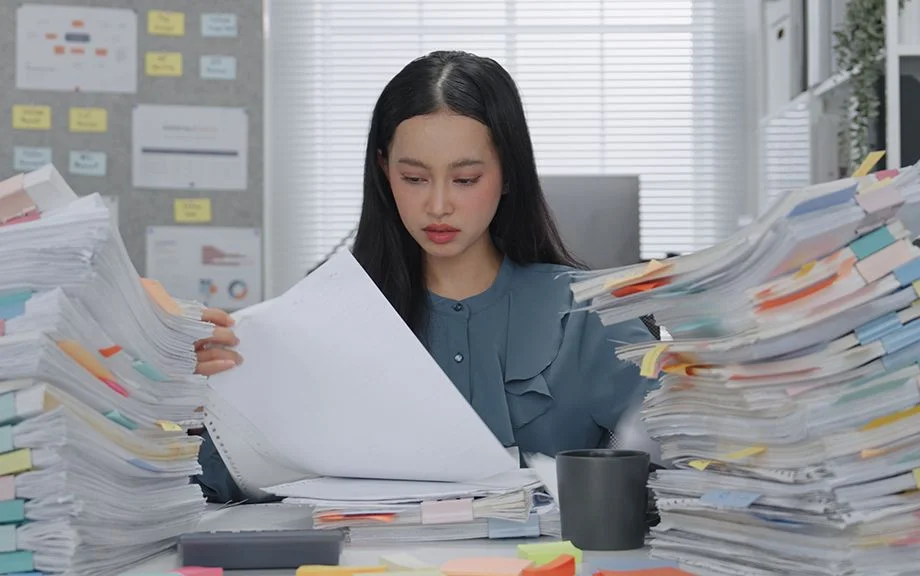 Asian Business woman working busy with massive stacks of documents check and review preparation data report or organizing paperwork workplace stress and administrative overload