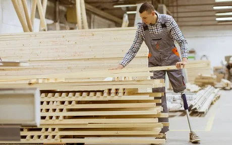Disabled young man with an artificial leg is working at the furniture factory