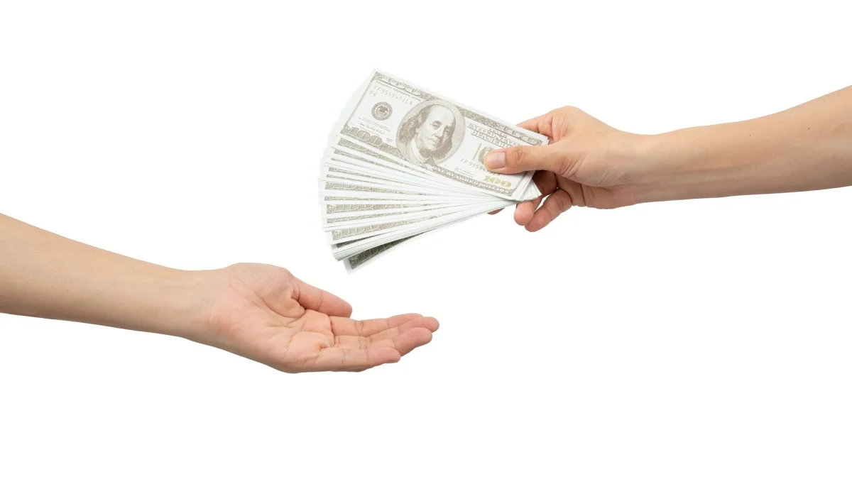 A hand exchanging bundles of cash, indicative of financial discussions.