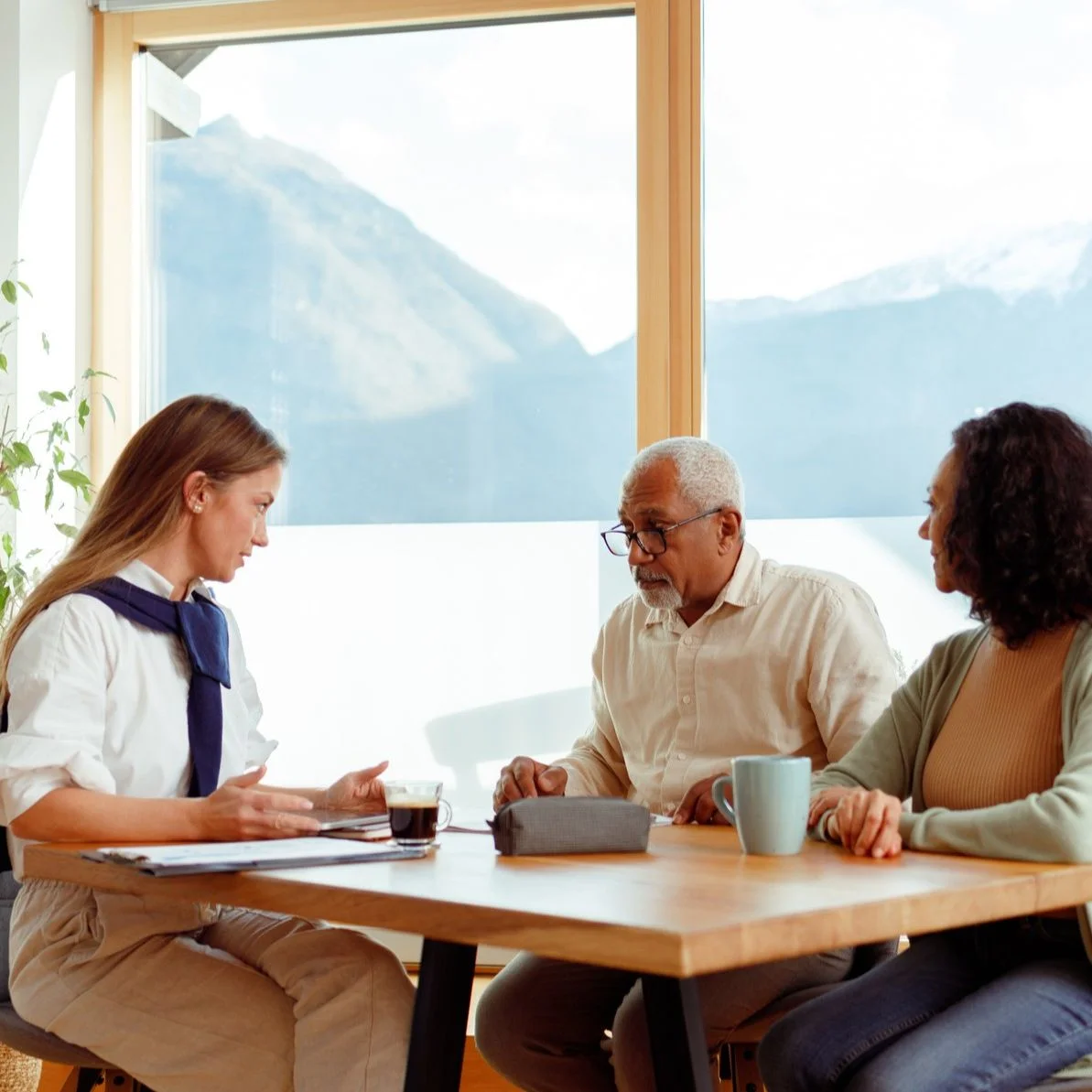A couple meets with a young woman at their kitchen table, paperwork spread out with a mountainous backdrop.
