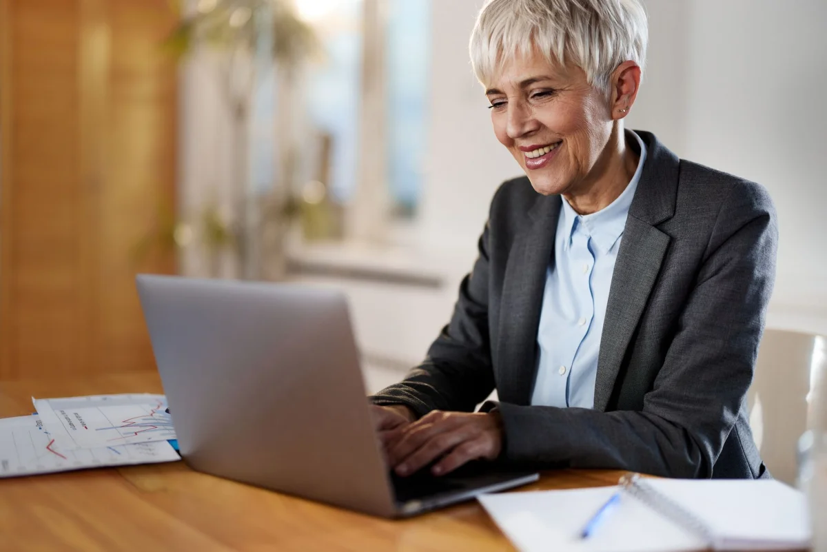 Happy senior businesswoman working on laptop at home office.