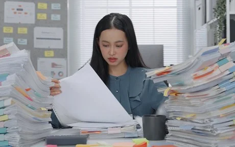 Asian Business woman working busy with massive stacks of documents check and review preparation data report or organizing paperwork workplace stress and administrative overload